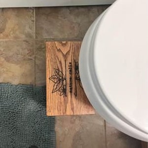 May include: Wooden toilet seat riser with the words "Rise and Shine" engraved on the top. The riser is made of natural wood and has a rustic look.