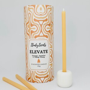 May include: A cylindrical container with a geometric pattern in shades of orange and white. The container is labelled "Study Scents Elevate Orange, Jasmine & Ylang-Ylang 25 Scented Candles 135g". Three yellow beeswax candles are shown next to the container.