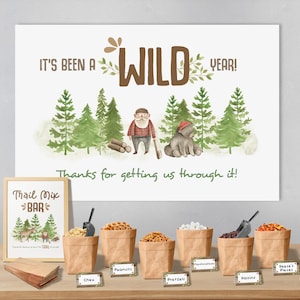 May include: A brown and white sign with the text "It's been a WILD YEAR!" and a cartoon illustration of a lumberjack and a bear in a forest setting. Below the sign is a table with a trail mix bar setup, featuring various snacks in brown paper bags with labels: Chex, Peanuts, Pretzels, Raisins, and Reese's Pieces.