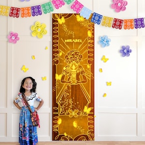 Può includere: Una porta di legno con un design luminoso di Mirabel del film Encanto, con il nome "MIRABEL" in alto. La porta è adornata da farfalle gialle e circondata da fiori e ghirlande di carta colorati.