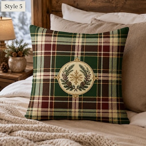 May include: A square throw pillow featuring a dark green, burgundy, and cream plaid pattern. Centered on the pillow is a circular emblem containing a gold snowflake, pine branches, and pinecones. The text Style 5 appears in the top left corner.