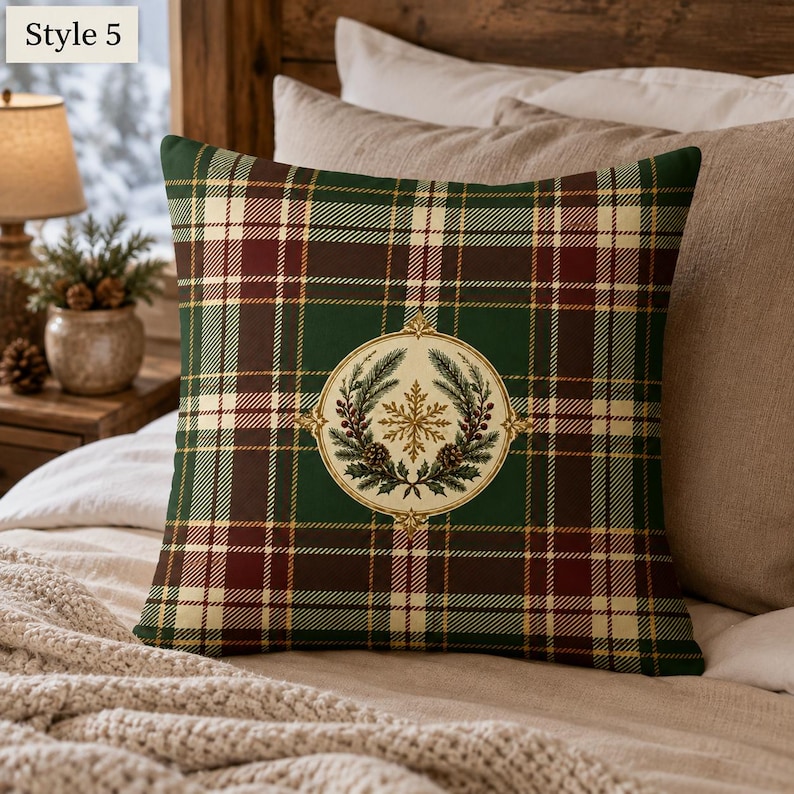 May include: A square throw pillow featuring a dark green, burgundy, and cream plaid pattern. Centered on the pillow is a circular emblem containing a gold snowflake, pine branches, and pinecones. The text Style 5 appears in the top left corner.