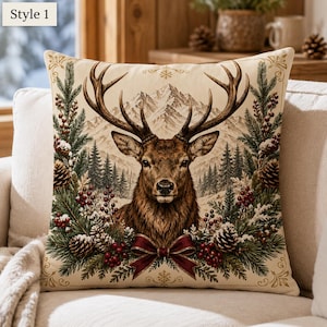 May include: A square throw pillow featuring a central illustration of a brown deer with large antlers, framed by green pine branches, red berries, and pinecones. The background depicts snow-capped mountains and a forest. The text Style 1 is visible.