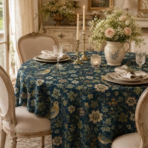 May include: A round tablecloth featuring a dark blue background with a repeating pattern of light-colored birds, white flowers, and green foliage. The table is set with white ceramic plates, clear glass tumblers, and a ceramic pitcher filled with flowers.