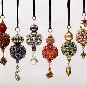 May include: Six beaded ornaments with different colours and designs, including red, blue, green, pink, and gold. Each ornament is suspended from a black string.