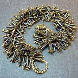 Peut inclure: Un collier de perles composé de perles dorées et gris foncé. Les perles sont disposées en un motif qui ressemble à une fleur.