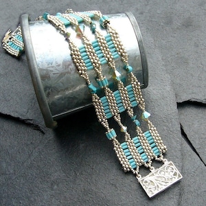 May include: A multi-strand bracelet with turquoise and silver beads, featuring a decorative silver clasp. The bracelet is displayed on a textured gray surface.