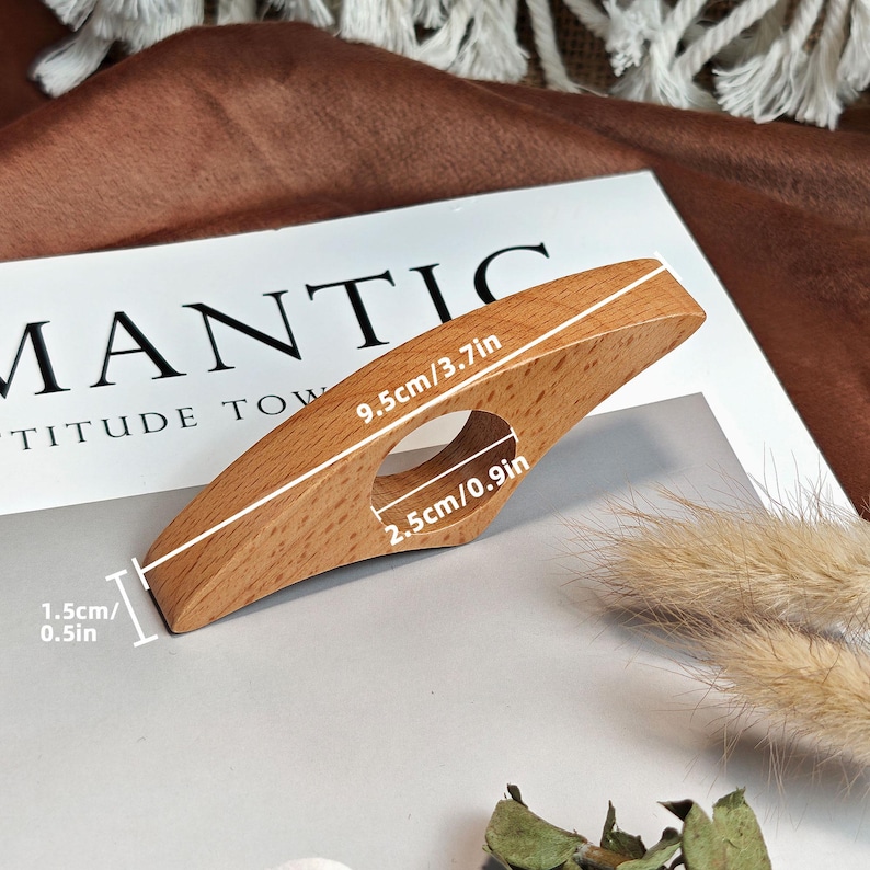 May include: A wooden book page holder, measuring 3.7 inches long, 0.9 inches wide, and 0.5 inches thick. The holder has a finger hole and is made of light-colored wood. The dimensions are clearly marked on the product.