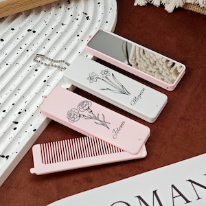 May include: A collection of personalized compact mirrors and hair combs. The mirrors and comb cases are pink and white, with floral illustrations and names. One mirror has a silver chain. The comb is pink.