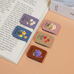 May include: Four colorful magnetic bookmarks with floral designs. The bookmarks are labeled with the names "Peggy", "Caroline", "Olivia", and "Sophia".