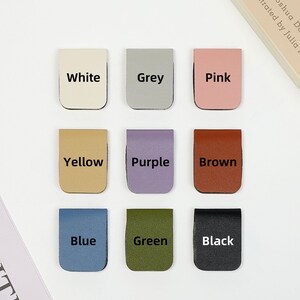 May include: Nine leather bookmark tabs in different colors: white, grey, pink, yellow, purple, brown, blue, green, and black. Each tab has the color name printed in black.