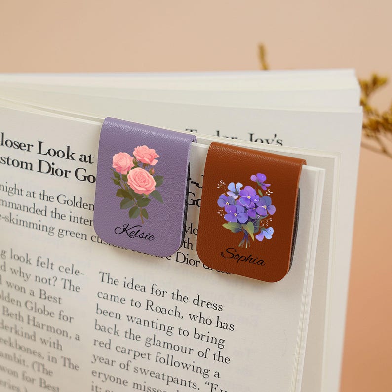 May include: Two personalized leather bookmark magnets with floral designs. The purple magnet features pink roses and the name Kelsie. The brown magnet features purple flowers and the name Sophia.