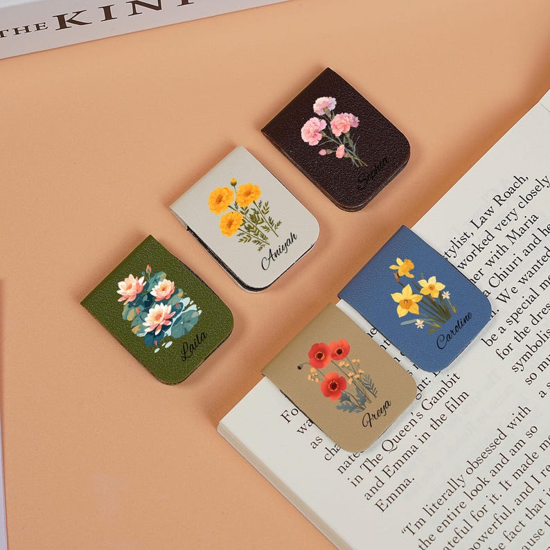 May include: Five colorful leather bookmark magnets with floral designs and personalized names. The bookmarks are in shades of brown, green, beige, white, and blue.