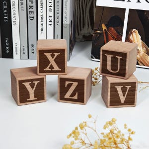 May include: Wooden alphabet blocks with the letters X, Y, Z, U, and V. The blocks are light brown with dark brown letters. The blocks are arranged on a white surface with books in the background.