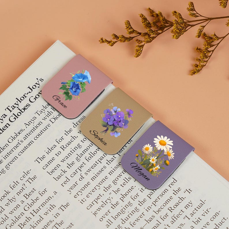 May include: Three magnetic bookmarks with floral designs and personalized names. The bookmarks are pink, beige, and purple with different floral patterns. The names "Grace", "Sophia", and "Megan" are printed on the bookmarks.