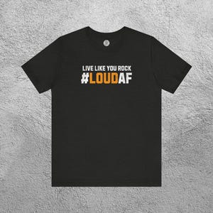 May include: Black t-shirt with the text "LIVE LIKE YOU ROCK #LOUDAF" in white and orange lettering. The shirt has a crew neck and short sleeves. The design is centered on the front of the shirt.