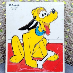 May include: Vintage Playskool wooden puzzle featuring Pluto the dog from Disney. The puzzle has 7 pieces and is recommended for children ages 2 to 4 years old. The puzzle shows Pluto sitting on a red floor with a bone.