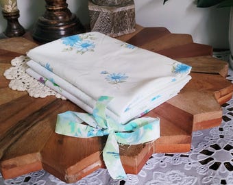 May include: A stack of three white fabric squares with a blue floral pattern. The fabric is tied together with a blue and green ribbon.