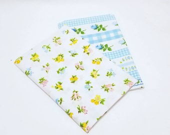 May include: Two pieces of fabric, one with a white background and a small floral pattern in yellow, pink, and blue, and the other with a blue and white gingham pattern.
