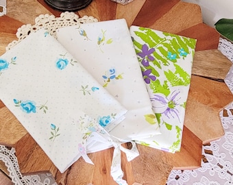 May include: Three fabric squares with floral patterns. The first square has a white background with blue flowers and white polka dots. The second square has a white background with blue and green flowers. The third square has a white background with green leaves and purple flowers.