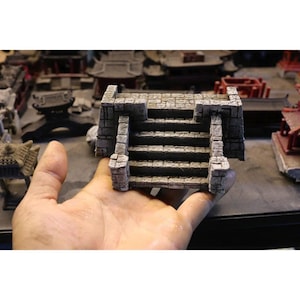 May include: A miniature stone staircase model featuring a weathered grey finish with a textured brick pattern. The structure includes two side pillars and three steps leading to a flat landing, designed for tabletop gaming terrain and dioramas.