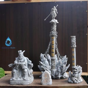 May include: A set of grey stone sculptures, featuring a seated figure, a tall column topped with a warrior statue, and a smaller column with a dragon base. A small stone tablet with gold text is also present. The sculptures are displayed on a wooden surface.