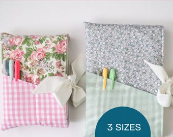 May include: Two fabric book sleeves with pockets, one with a pink gingham pocket and floral print, the other with a green and white gingham pocket and floral print. The text "IORA BOOK SLEEVE" and "3 SIZES INCLUDED!" are visible.