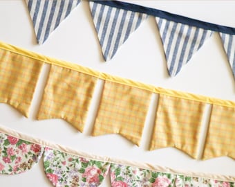 May include: Three rows of decorative bunting in various patterns. The top row features blue and white striped triangles. The middle row has yellow plaid rectangles. The bottom row displays a floral pattern with pink roses. Text at the top reads "FETE BUNTING", "HANDMADE BEGINNINGS", and "SEWING PATTERN".
