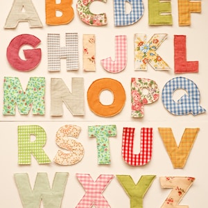 May include: A collection of colorful fabric letters, each with a unique pattern. The letters are arranged in alphabetical order, featuring various designs like floral, gingham, and solid colors. Ideal for crafting or educational purposes.