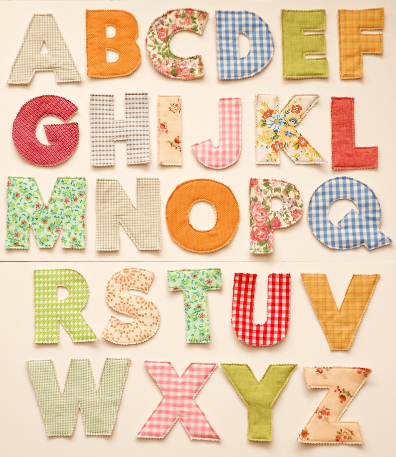 May include: A collection of colorful fabric letters, each with a unique pattern. The letters are arranged in alphabetical order, featuring various designs like floral, gingham, and solid colors. Ideal for crafting or educational purposes.