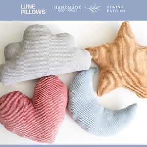 May include: Four corduroy pillows shaped like a cloud, star, heart, and crescent moon. The cloud is grey, the star is tan, the heart is red, and the moon is light blue. The text "Lune Pillows" is at the top left.