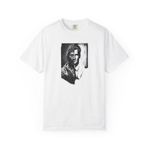 May include: A white short-sleeved t-shirt featuring a central black and white graphic print. The design displays a split-face portrait, showing a rugged individual with a beanie on the left and a clean-shaven person in a suit on the right.