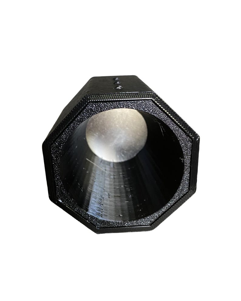 May include: A black, octagonal-shaped object with a textured surface. The object has a large, circular opening at one end and a smaller opening at the other. The interior is a smooth, dark surface. The object appears to be made of plastic.