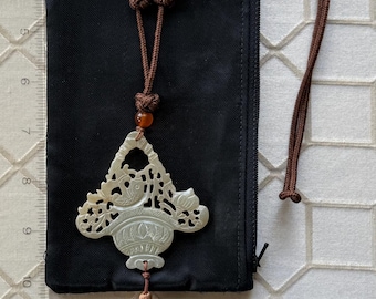 Op de afbeelding: Lichtgroene hanger met een vogel- en bloemmotief, hangend aan een bruin koord met tijgeroog kralen. Een bruine kwast hangt onder de hanger. De hanger rust op een zwarte stoffen etui.