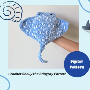 May include: A light blue and white crocheted stingray plush toy with a textured yarn finish, dark eyes, and a long tail. The image includes the text "Digital Pattern" and "Crochet Shelly the Stingray Pattern" in a clear, readable font style.