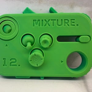 May include: A green plastic device with the word "MIXTURE." printed on it. It has four knobs, a slider, and a large hole. The number "12." is printed on the device.