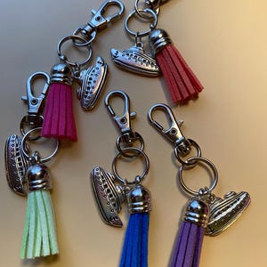 May include: A collection of keychains featuring silver-toned cruise ship charms and colorful tassels. The tassels come in shades of pink, red, green, blue, and purple. Each keychain has a silver clasp and a metal ring.