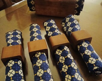 May include: A set of navy blue and white patterned cloth napkins with wooden napkin rings. A matching napkin holder is also present. The napkins have a repeating pattern of white circles with yellow accents on a dark blue background. The napkin rings are square and made of wood.