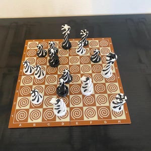 Könnte beinhalten: Schachspiel mit schwarz-weiß gestreiften Zebrafiguren auf einem braun-beigen Brett. Das Brett hat in jedem Feld ein Spiralmuster. Die Figuren sind so angeordnet, als ob ein Spiel im Gange ist.