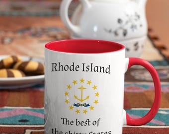 May include: White ceramic mug with a red interior and handle. The mug features the text "Rhode Island" above a yellow anchor emblem surrounded by stars, and the phrase "The best of the shitty States."