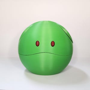 May include: A spherical, lime green object with two red, oval-shaped eyes and a black, curved line beneath them. The object has a seam running around its circumference and a diagonal line on its side. The background is plain white.