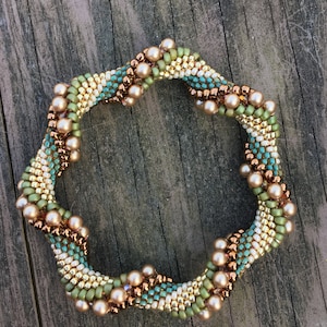 K&ouml;nnte beinhalten: Ein Armband mit Perlen in Spiralform. Das Armband besteht aus kleinen, goldenen, gr&uuml;nen und blauen Perlen. Das Armband ist mit gr&ouml;&szlig;eren, kupferfarbenen Perlen verziert.