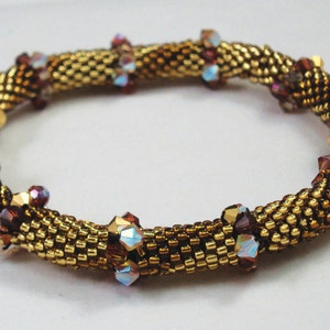 May include: A gold and brown beaded bracelet with iridescent crystals. The bracelet is made with small seed beads and larger faceted crystals.
