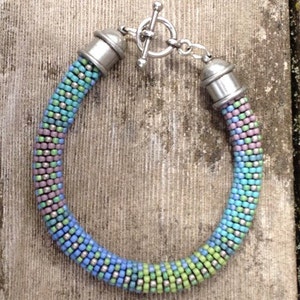 May include: A multi-colored beaded bracelet with a silver toggle clasp. The bracelet is made with small, round beads in shades of blue, green, purple, and silver.