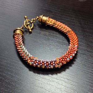May include: A beaded bracelet with a gradient of orange, pink, and purple beads. The bracelet has a brass clasp.