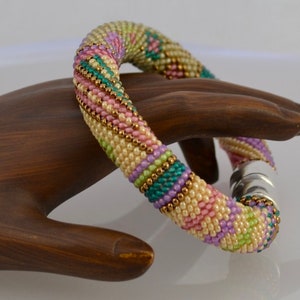 May include: A multi-coloured beaded bracelet with a magnetic clasp. The bracelet is made with small, round beads in shades of pink, green, gold, and white.