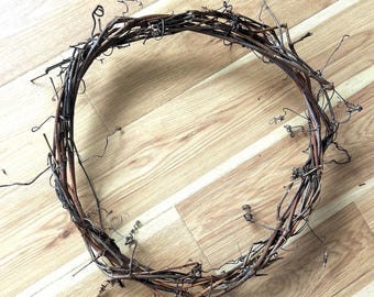 May include: A circular grapevine wreath, featuring a natural, rustic design. The wreath is composed of intertwined brown and tan branches, with delicate tendrils extending outwards. This decorative wreath is suitable for seasonal home decor.