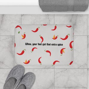 Könnte beinhalten: Weiße Badematte mit roten Chilischoten-Illustrationen und dem Text "Whoa, your feet got that extra spice".