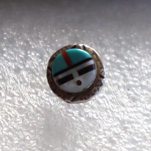 May include: A circular stud earring featuring a silver metal frame with a textured edge. The center inlay consists of a polished stone mosaic with a turquoise blue top section, a thin red vertical stripe, and horizontal black and white bands.