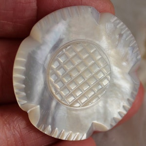 Può includere: Bottone a forma di fiore perlato con centro strutturato e bordi smerlati. Il bottone ha un aspetto iridescente che riflette la luce. Il design ricorda un fiore stilizzato, adatto per cucito o progetti di artigianato. Misura circa 4 cm di diametro.